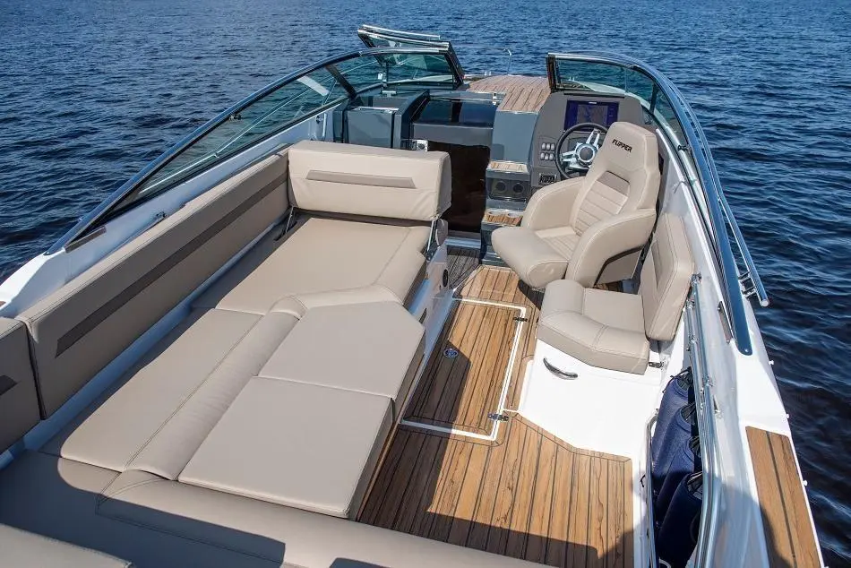 Stylish boat interior featuring beige seating and wooden flooring, with a view of calm water and modern dashboard controls.